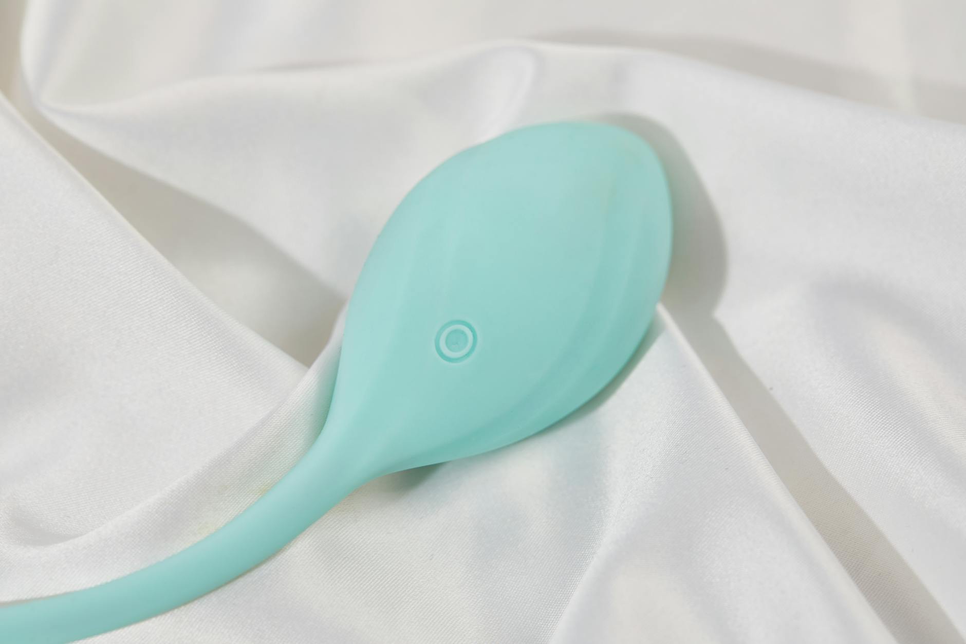 A teal silicone lemon clitoral vibrator on smooth white silk, representing body-safe intimate wellness.