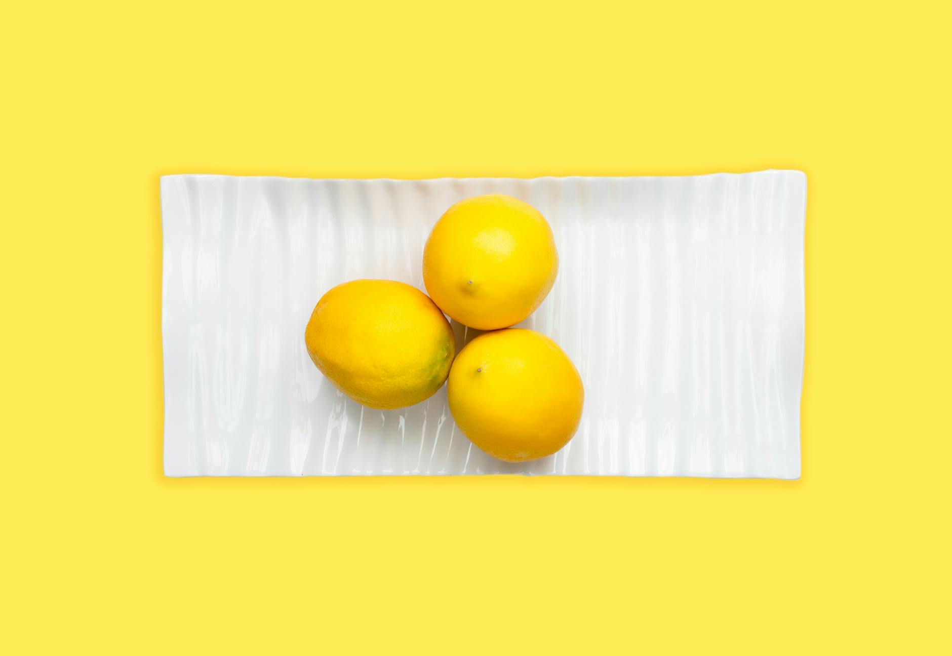 Fresh lemons arranged on a white plate against a vibrant yellow background, representing the sensory exploration of lemon vibrators