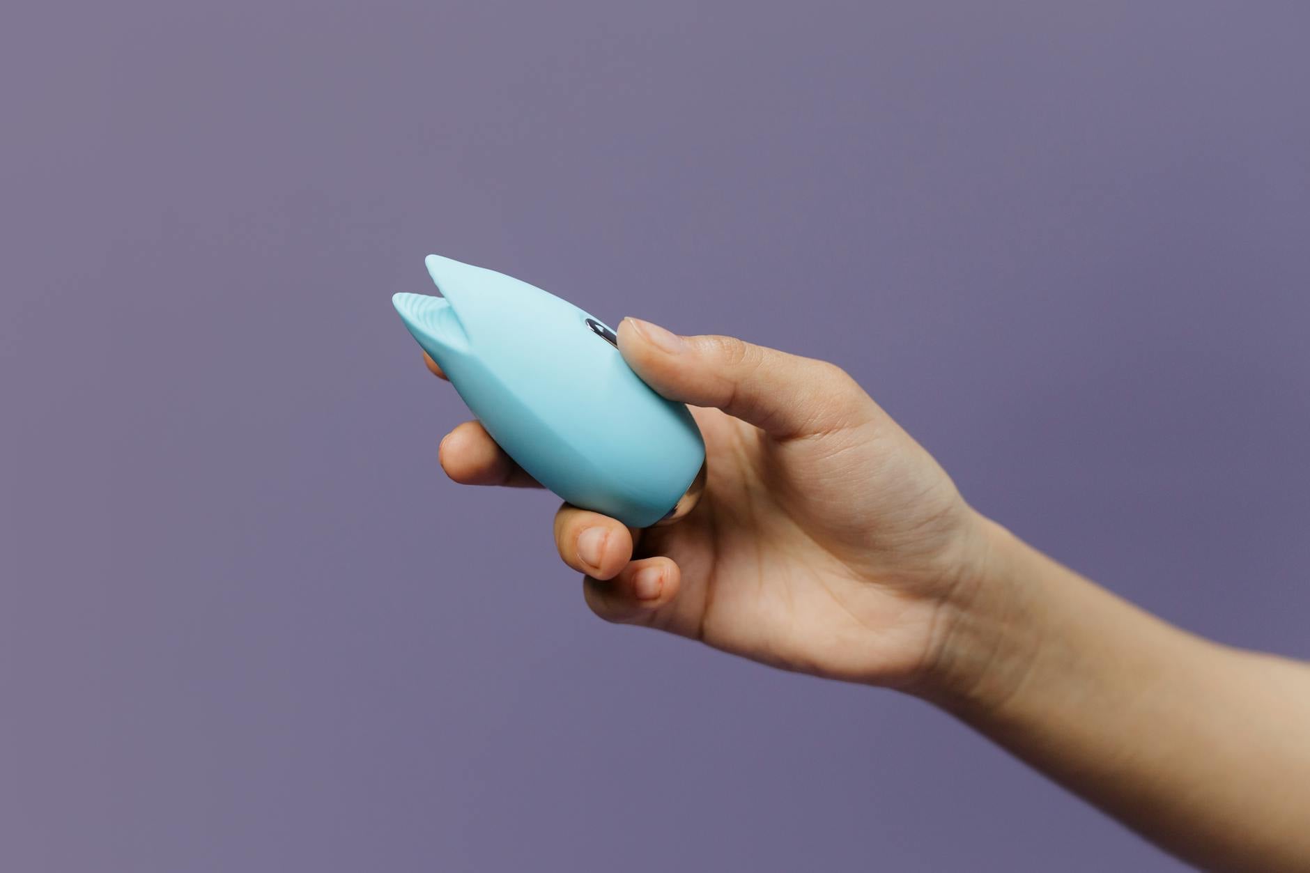 40代女性の手に握られた青いシリコンバイブレーター。背景は紫。自分へのケアとセクシュアリティを表現している。