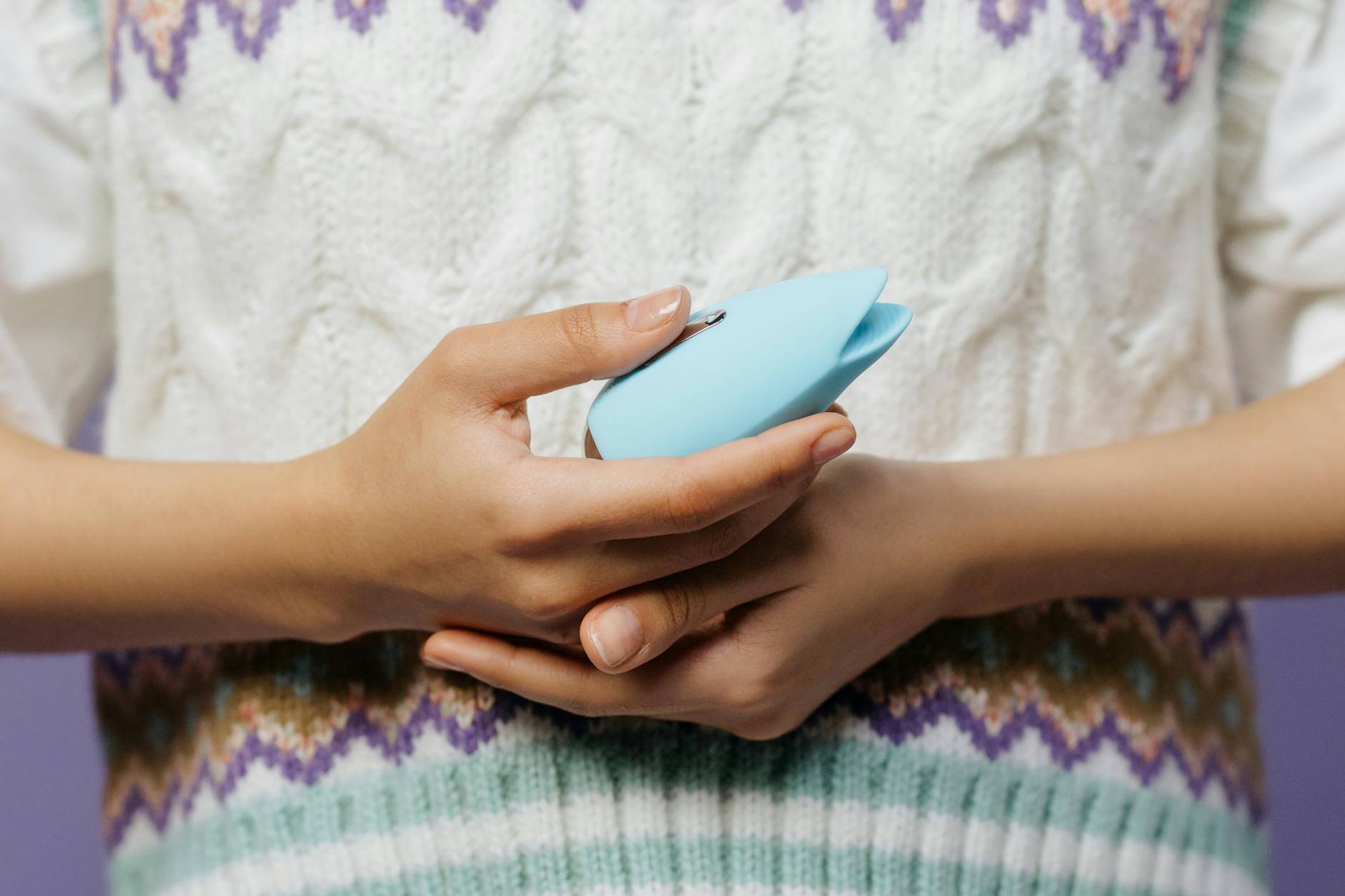 Two hands holding pink and blue silicone vibrators against a pastel background.